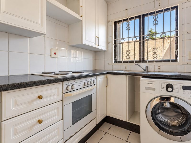 A functional kitchen featuring white cabinetry, granite countertops, a built-in oven and hob, and a tiled backsplash with a window security gate.