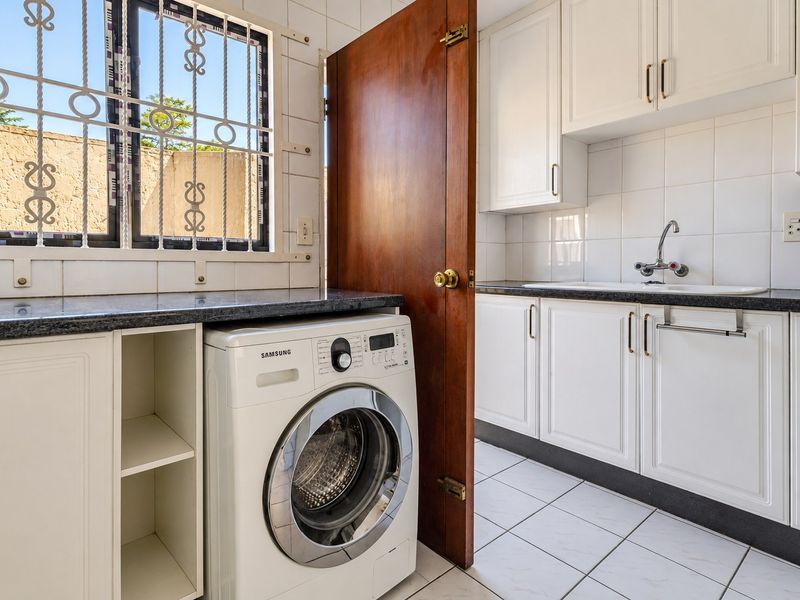 A functional laundry area featuring built-in white cabinetry, granite countertops, a sink, and tiled finishes, providing practical utility space.