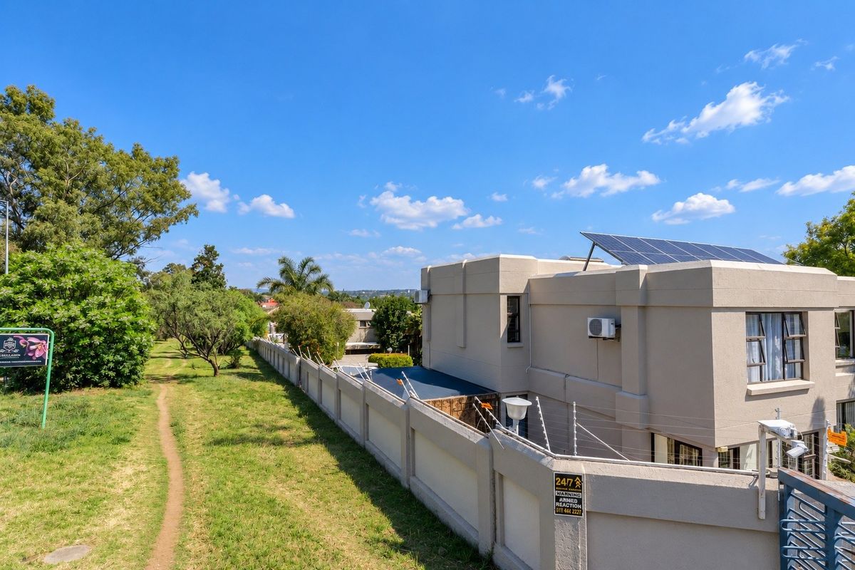 Rear view of the property featuring a perimeter wall with electric fencing, security cameras, and roof-mounted solar panels.