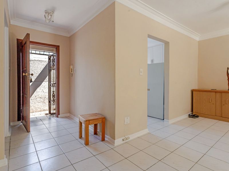 A bright entrance area featuring neutral wall tones, tiled flooring, decorative cornicing, and a secure exterior door with an integrated security gate.