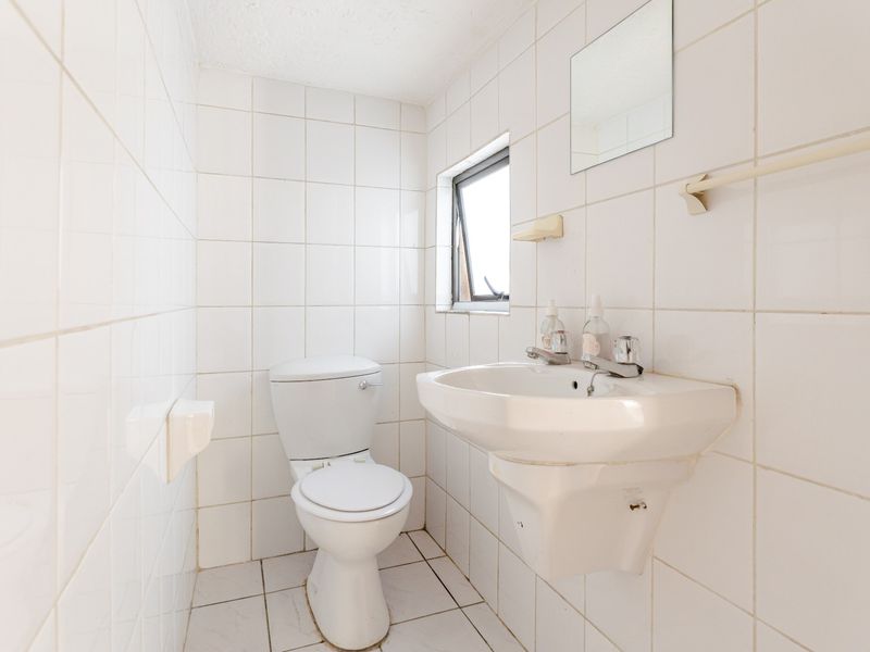 A compact bathroom featuring white wall-mounted basin, toilet, and fully tiled surfaces, offering a functional space ready for modernization.