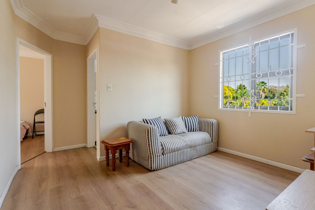 A well-maintained bedroom featuring laminate flooring, decorative cornice, and a window fitted with security bars.