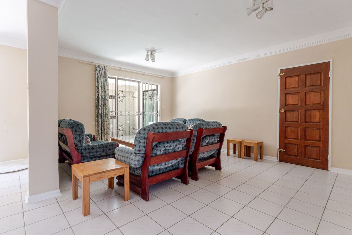 A spacious living room featuring neutral tiled flooring, a wooden panel door, and a sliding glass door with security gate leading to the exterior.