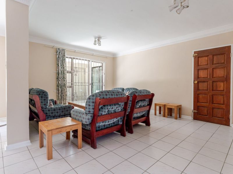 A spacious living room featuring neutral tiled flooring, a wooden panel door, and a sliding glass door with security gate leading to the exterior.