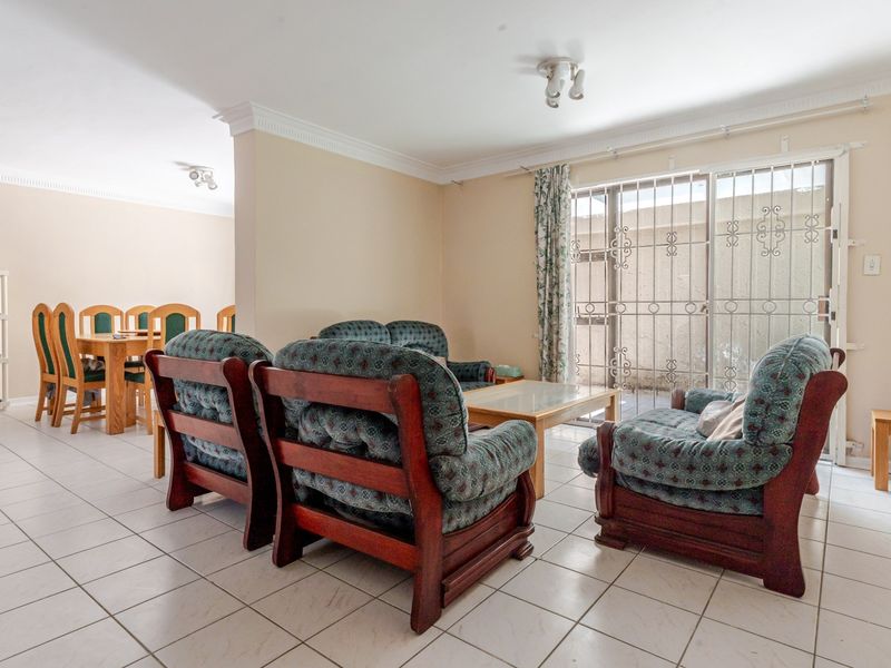 Open plan living and dining area featuring tiled flooring, ceiling cornices, and a sliding glass door with security gate leading to the exterior.