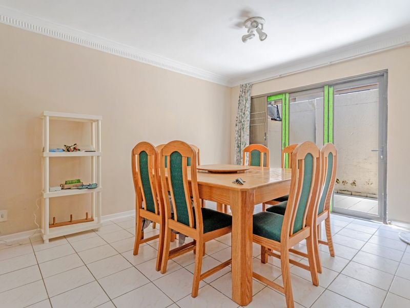 A functional dining area featuring tiled flooring, ceiling cornice detailing, and a sliding glass door providing access to the outdoor patio space.