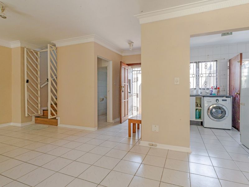 Open plan living area featuring tiled flooring, a staircase with security gate, and an adjacent kitchen area with built-in cabinetry.