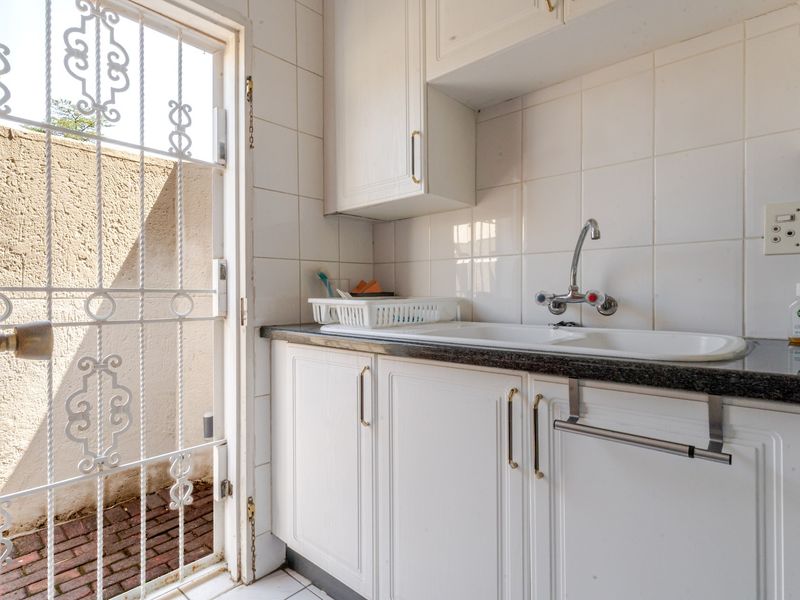 A functional scullery area featuring built-in white cabinetry, a double sink with mixer tap, and tiled splashbacks, with direct access to an outdoor area.