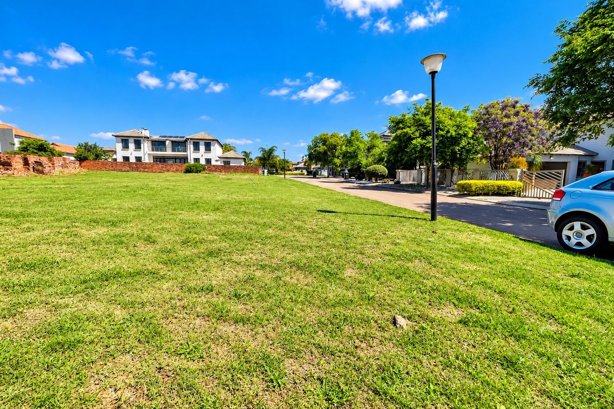 A vacant residential plot featuring a well-maintained grass lawn, bordered by a brick wall, situated in a developed neighborhood setting.