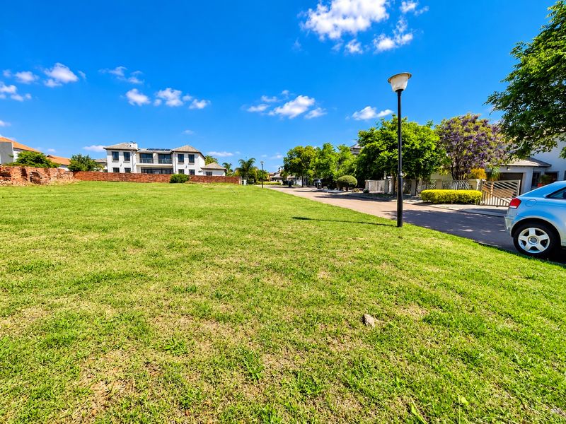 A vacant residential plot featuring a well-maintained grass lawn, bordered by a brick wall, situated in a developed neighborhood setting.