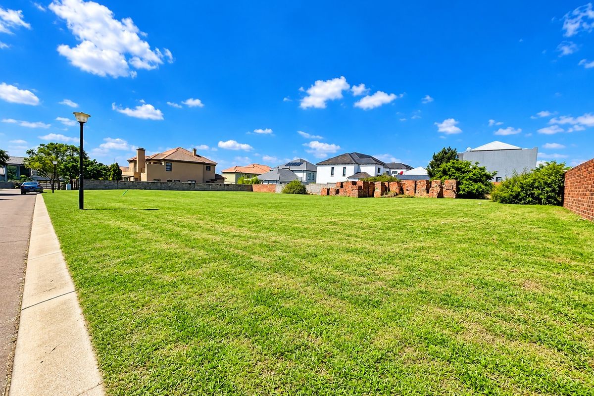 A vacant residential plot featuring a well-maintained lawn, boundary wall, and street light, situated in a developed neighborhood.