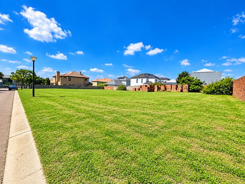A vacant residential plot featuring a well-maintained lawn, boundary wall, and street light, situated in a developed neighborhood.