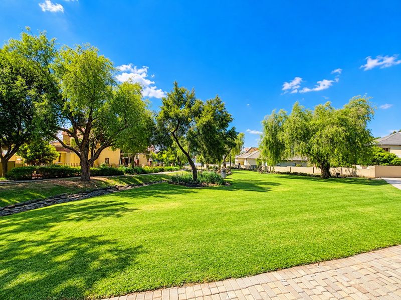 A well-maintained residential garden featuring a lush green lawn, mature trees, and a stone-lined drainage feature, providing a serene outdoor space.
