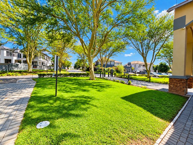 A well-maintained residential garden area featuring a manicured lawn, mature trees, and paved driveway access within a secure estate setting.