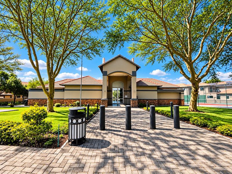 A well-maintained clubhouse building featuring stone cladding, a tiled roof, and a paved entrance path surrounded by mature trees and landscaped gardens.