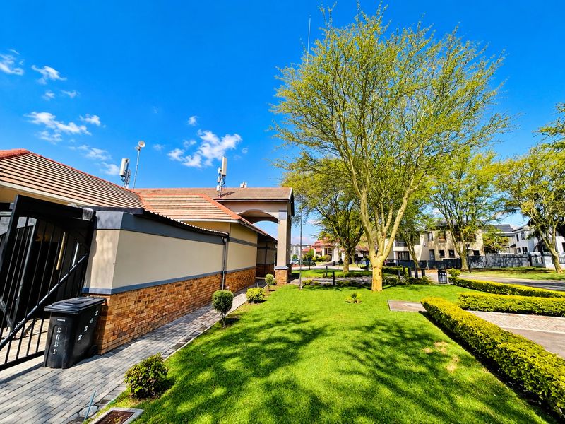 A well-maintained residential exterior featuring a brick and plaster facade, tiled roof, paved walkway, and manicured garden area with mature trees.