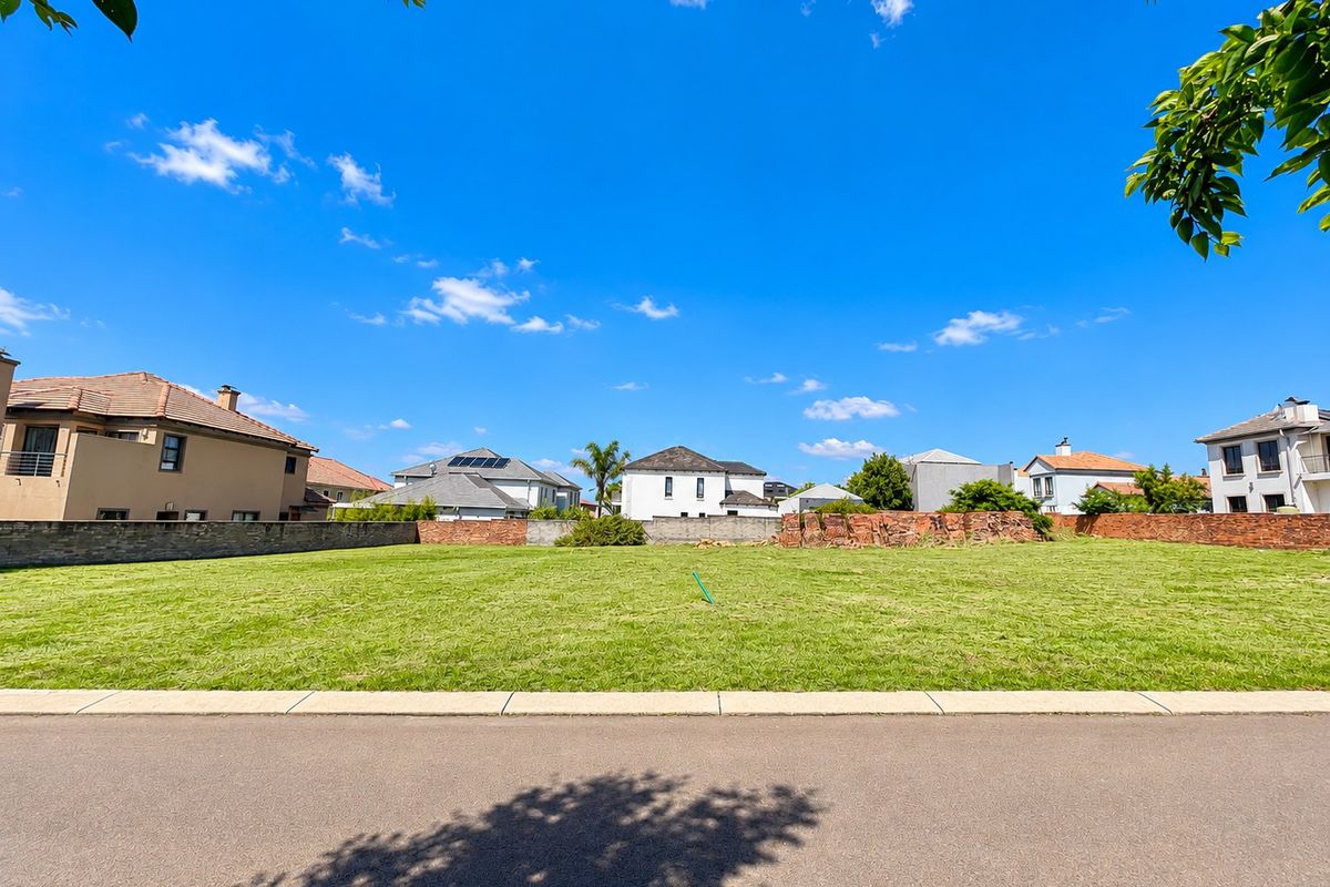 A vacant residential plot featuring a level grassed area, paved road frontage, and existing boundary walls in a developed neighborhood.