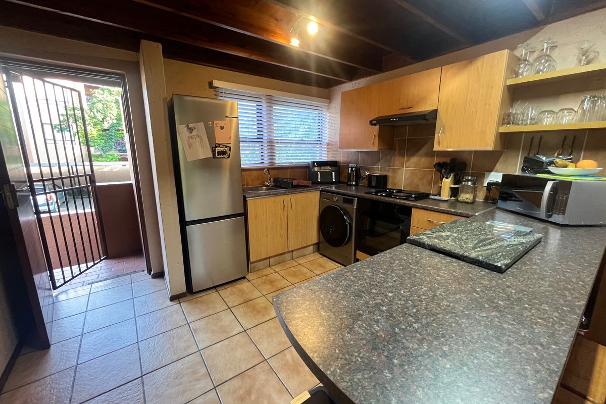 A functional kitchen featuring laminate cabinetry, dark countertops, tiled flooring, and exposed timber ceiling beams, with direct access to an outdoor balcony area.