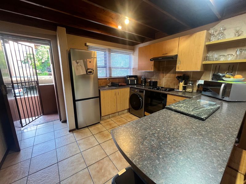 A functional kitchen featuring laminate cabinetry, dark countertops, tiled flooring, and exposed timber ceiling beams, with direct access to an outdoor balcony area.