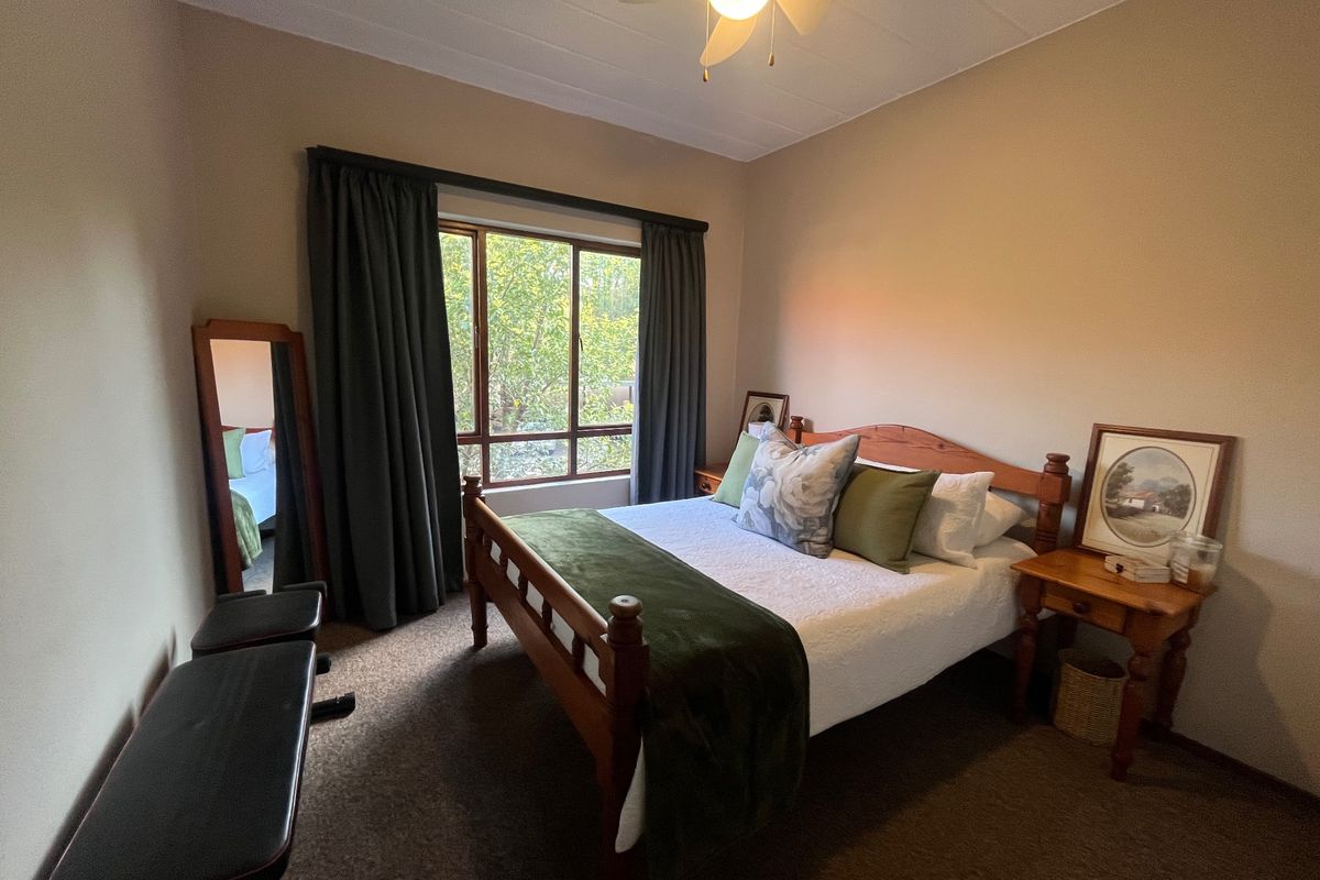 A cozy bedroom featuring carpeted flooring, a ceiling fan, and a large window that provides natural light and a view of the greenery outside.