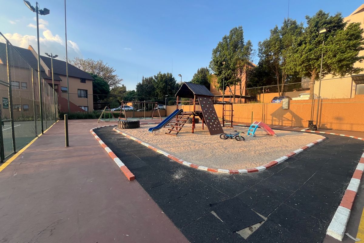 Communal outdoor playground area featuring sand pit, climbing frame, slide, and perimeter fencing within an apartment complex.