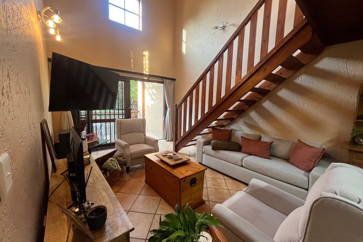 Spacious living room featuring high vaulted ceilings, terracotta floor tiles, and a wooden staircase leading to the upper level, with access to a patio.