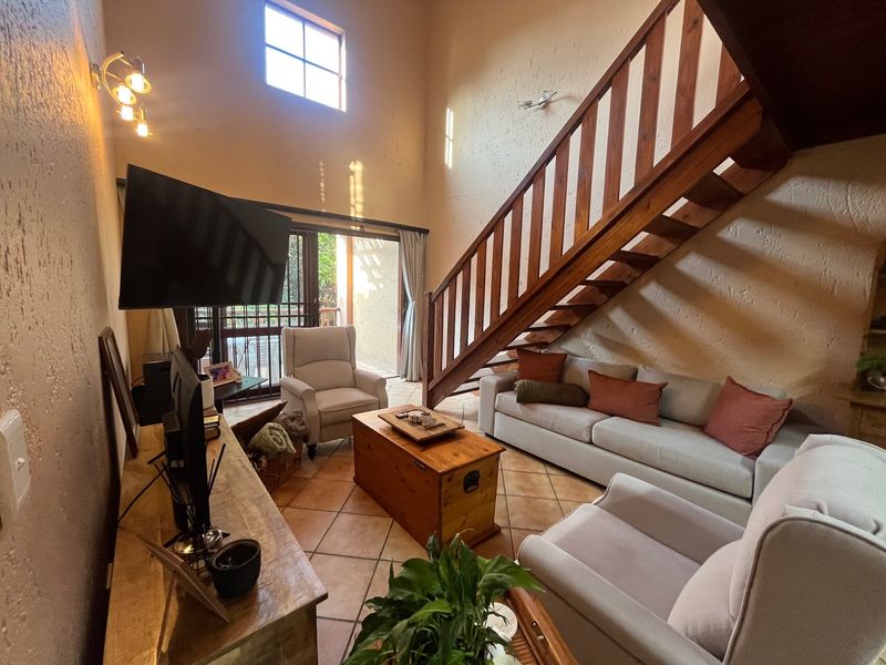 Spacious living room featuring high vaulted ceilings, terracotta floor tiles, and a wooden staircase leading to the upper level, with access to a patio.