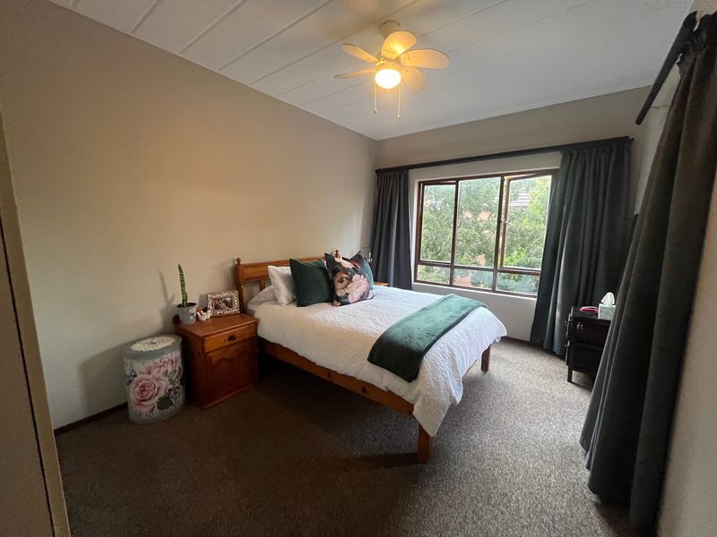 A comfortable bedroom featuring carpeted flooring, a ceiling fan, and a large window providing natural light and garden views.