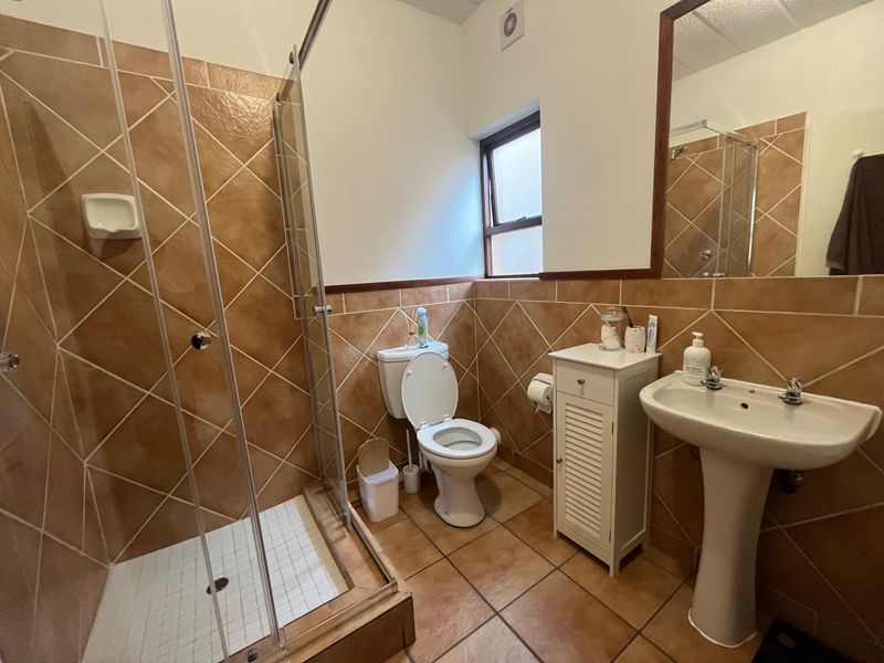 A functional bathroom featuring a shower enclosure, pedestal basin, and toilet, finished with neutral-toned wall and floor tiles.