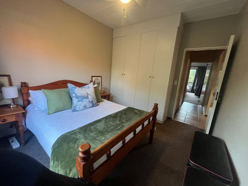 A cozy bedroom featuring built-in cupboards, a ceiling fan, and carpeted flooring, with direct access to the hallway.