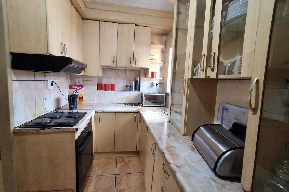 A functional kitchen featuring light-toned built-in cabinetry, laminate countertops, an integrated electric hob and oven, and tiled finishes throughout.
