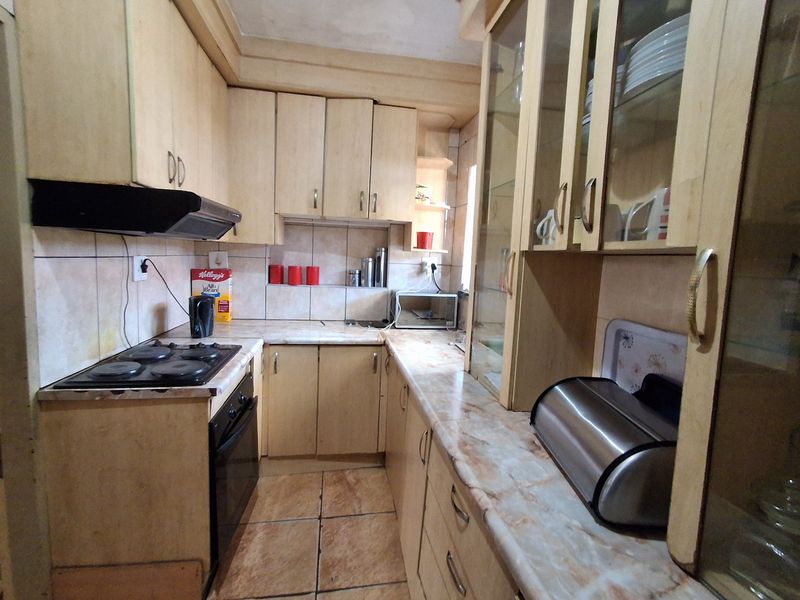 A functional kitchen featuring light-toned built-in cabinetry, laminate countertops, an integrated electric hob and oven, and tiled finishes throughout.