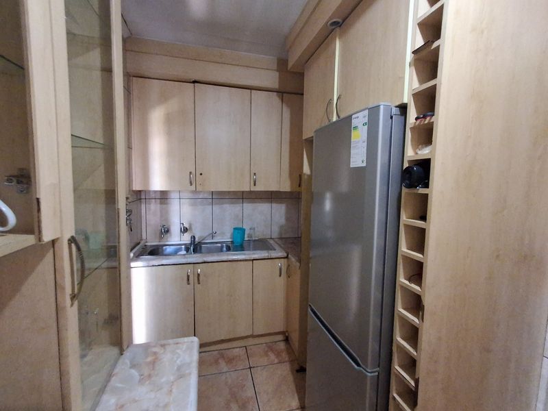 Compact kitchen featuring light wood-tone cabinetry, tiled backsplash, double basin sink, and integrated wine storage rack.