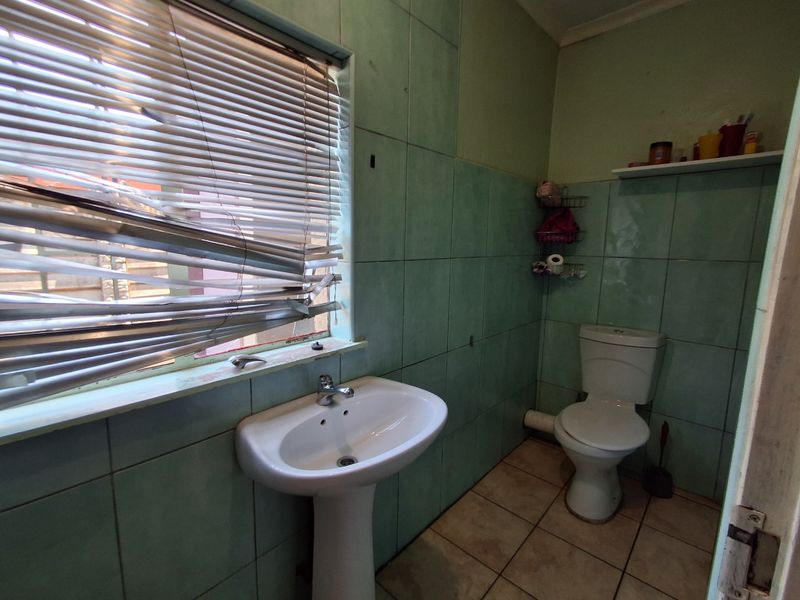 A functional bathroom featuring a pedestal basin and ceramic toilet, finished with green wall tiling and neutral floor tiles.