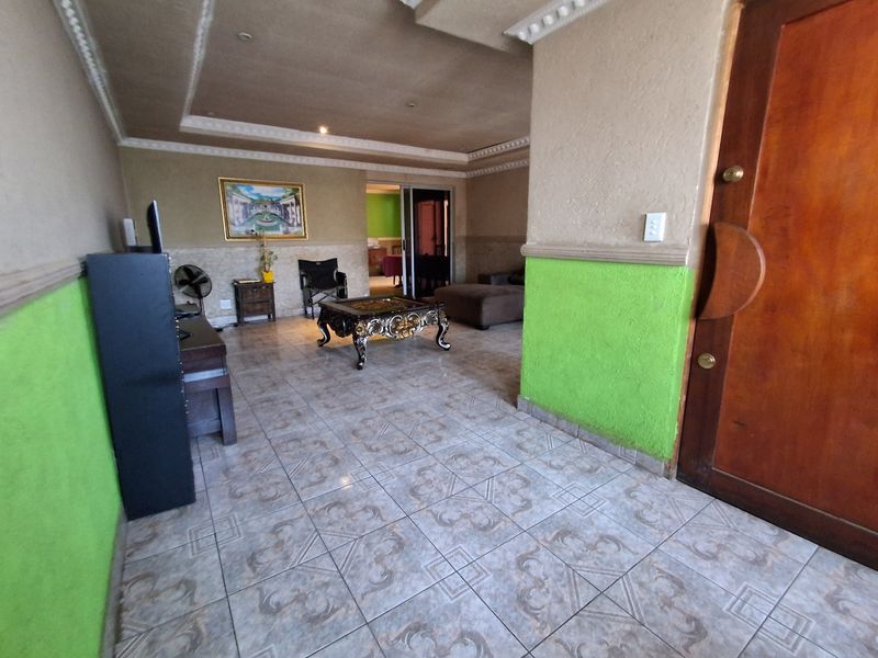 Spacious living area featuring tiled flooring, decorative ceiling molding, and a solid wood entrance door, offering a functional layout with potential for modernization.