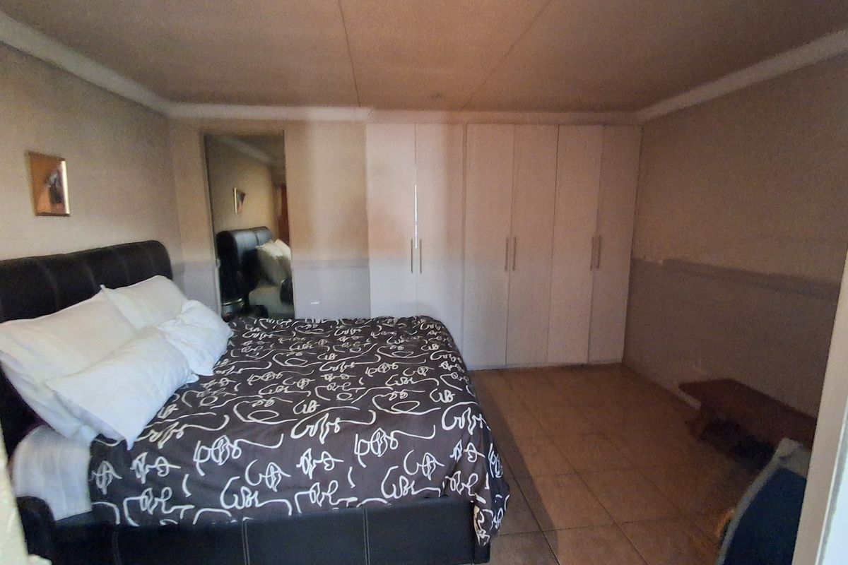 A bedroom featuring built-in cupboards, tiled flooring, and a mirrored closet door, currently requiring cosmetic updates to the walls and ceiling.