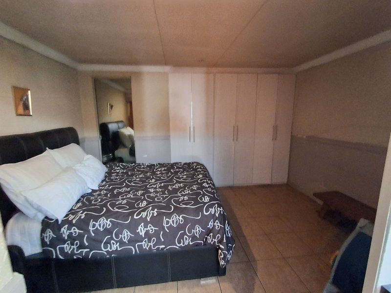 A bedroom featuring built-in cupboards, tiled flooring, and a mirrored closet door, currently requiring cosmetic updates to the walls and ceiling.