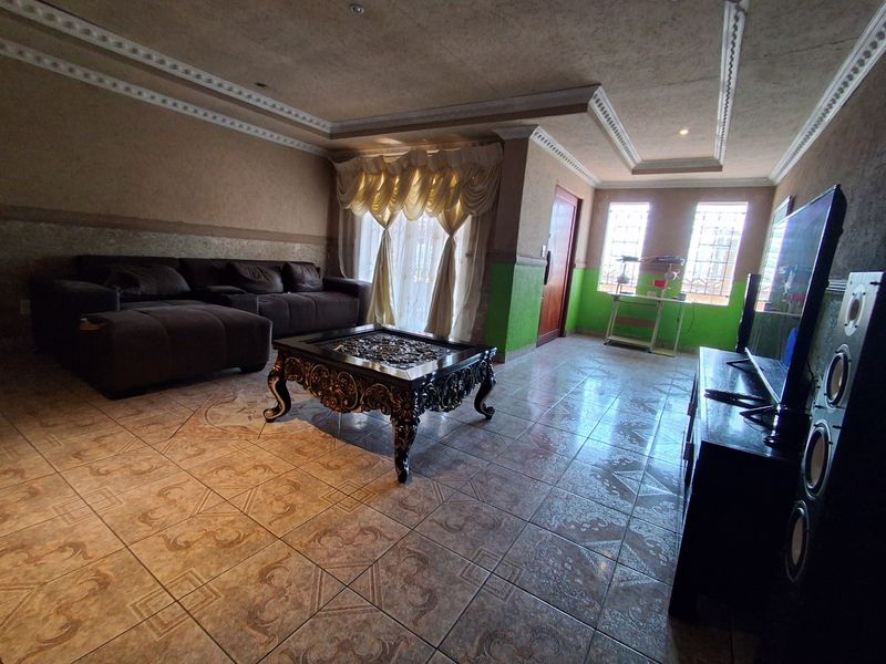 A spacious living room featuring tiled flooring, decorative ceiling molding with recessed lighting, and windows fitted with security bars.