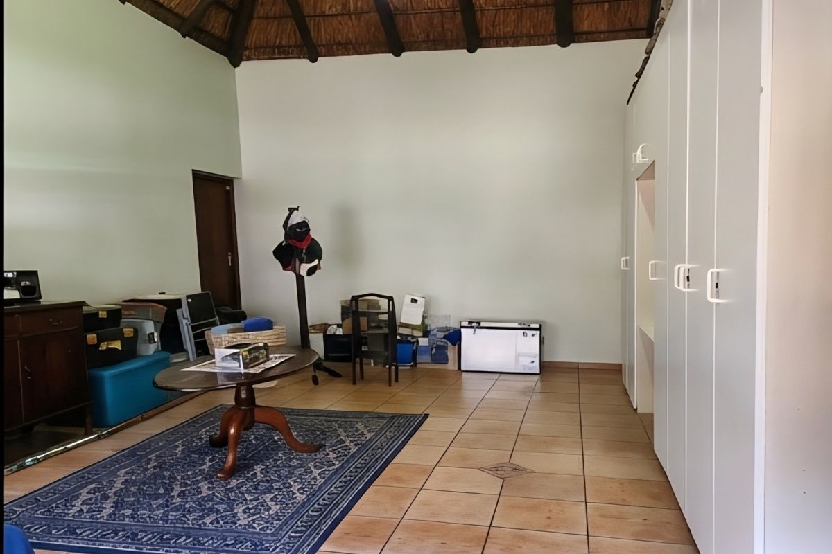 Spacious bedroom featuring a high vaulted thatched ceiling with exposed timber beams, tiled flooring, and extensive built-in cupboard storage.