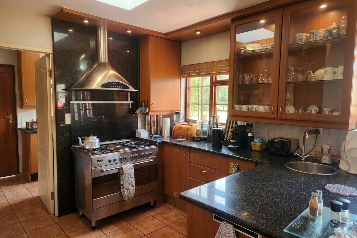 A functional kitchen featuring wooden cabinetry, granite countertops, a stainless steel gas stove with extractor, and a skylight providing natural light.
