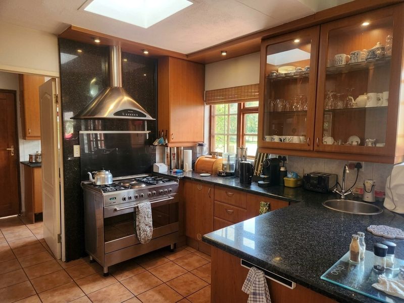 A functional kitchen featuring wooden cabinetry, granite countertops, a stainless steel gas stove with extractor, and a skylight providing natural light.