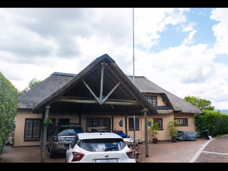 A charming house featuring a traditional thatch roof and a spacious timber-framed carport, set on a well-maintained paved driveway with established garden hedging.