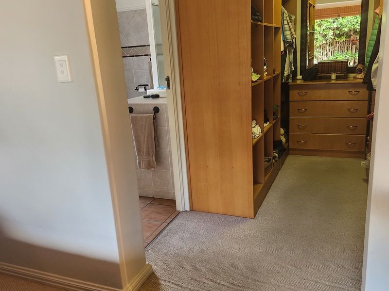 A bedroom walk-in closet area featuring built-in wooden shelving and carpeted flooring, with an adjacent view into a tiled bathroom.
