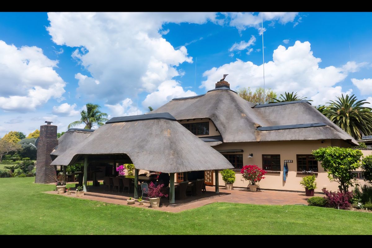 Rear view of a charming house featuring a traditional thatched roof, a spacious covered patio area, and a well-maintained garden.