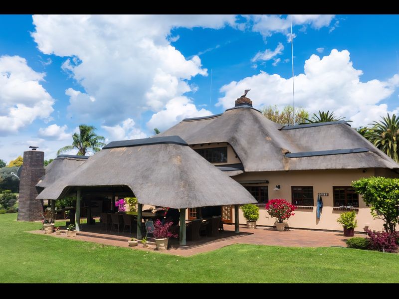 Rear view of a charming house featuring a traditional thatched roof, a spacious covered patio area, and a well-maintained garden.