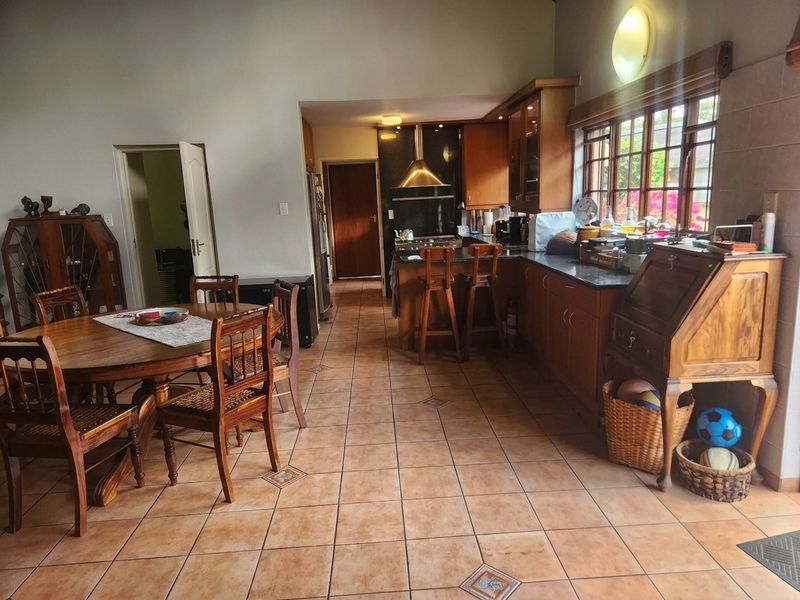 Spacious open-plan kitchen and dining area featuring tiled floors, warm wooden cabinetry, granite countertops, and ample natural light from large multi-pane windows.