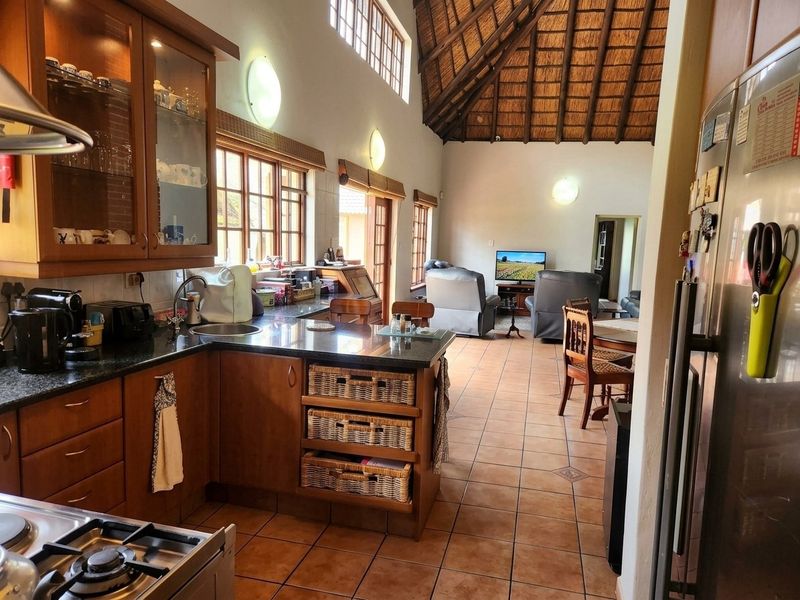 Open-plan kitchen and living area featuring timber cabinetry, granite countertops, tiled flooring, and a high-vaulted thatched ceiling with exposed timber beams.