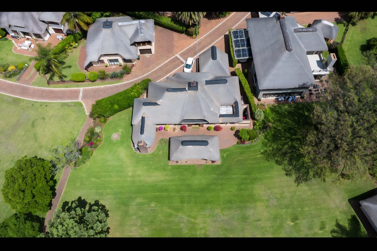 Aerial view of a residential property featuring a thatched roof, solar panels, and a spacious landscaped garden within a well-maintained estate setting.