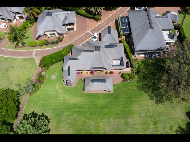 Aerial view of a residential property featuring a thatched roof, solar panels, and a spacious landscaped garden within a well-maintained estate setting.