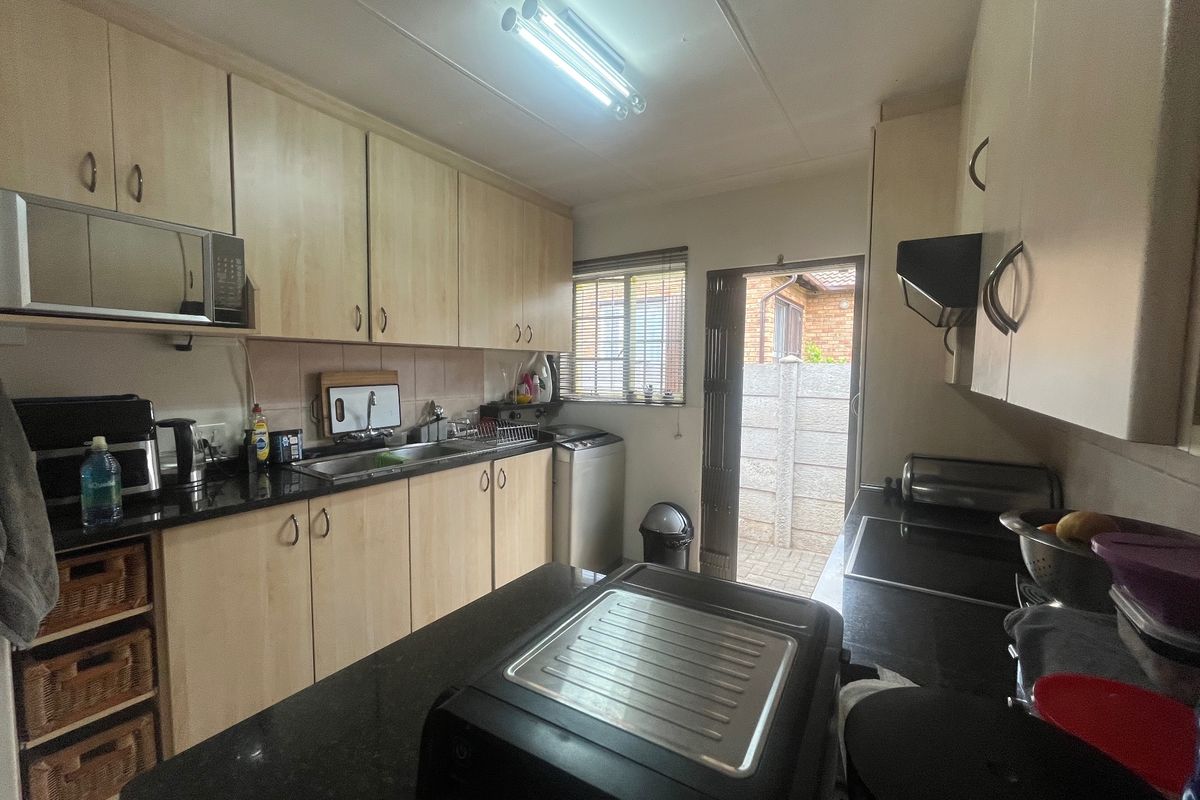 Functional kitchen featuring light wood cabinetry, dark granite countertops, integrated appliances, and direct access to an exterior paved area.